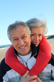 Senior man giving piggyback ride to woman by the sea