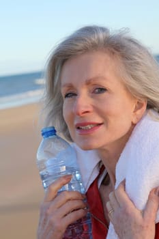 Active senior woman drinking water from bottle at the beach