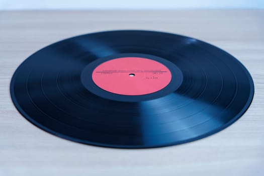 Classic black vinyl record with a red label lying on a wooden background. A nostalgic symbol of analog music, retro sound, and vintage audio formats