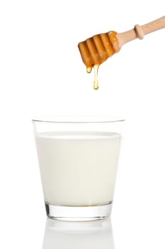 Honey dripping from a honey spoon into a glass of milk against a white background