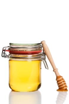 Honey spoon leaning against a jar with honey against a white background