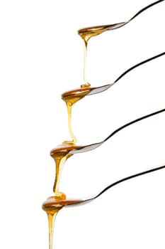 Honey flowing over four spoons against a white background