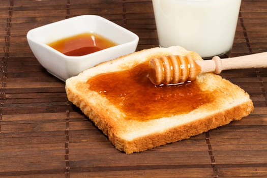 Honey spoon with honey on a toast,with a glass of milk and a bowl of honey