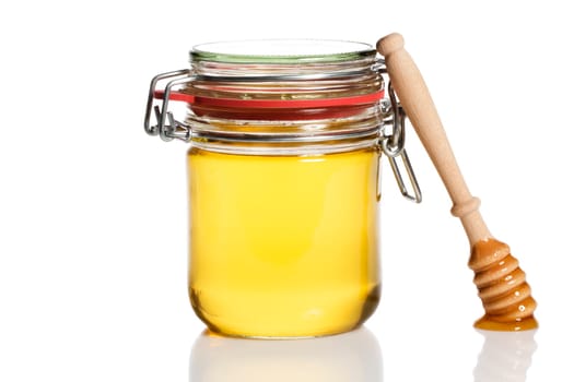 Honey spoon leaning against a jar with honey against a white background
