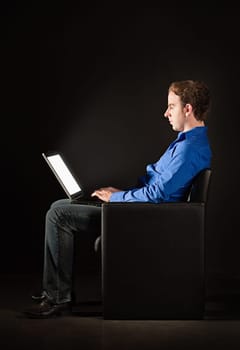 Young man sitting in the darkness with laptop, illuminated by the light from the screen