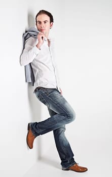 Full height portrait of young man leaning to a white wall