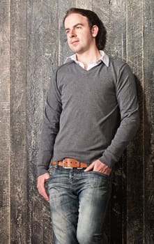Portrait of a young pensive guy leaning to a dark painted wooden wall