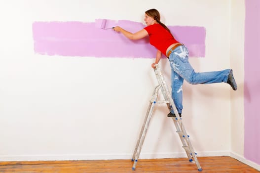 Young woman in a colorful T-shirt paints her first apartment with a paint roller.