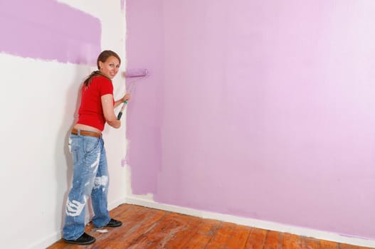 Young woman in a colorful T-shirt paints her first apartment with a paint roller.