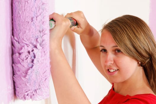 Young woman in a colorful T-shirt paints her first apartment with a paint roller.