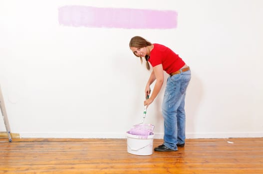 Young woman in a colorful T-shirt paints her first apartment with a paint roller.