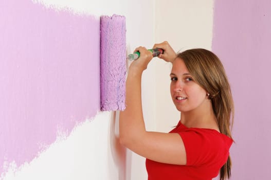 Young woman in a colorful T-shirt paints her first apartment with a paint roller.