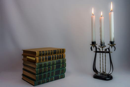 A stack of vintage hardcover books and an ornate antique candelabrum with burning candles, set in dim lighting, creating a nostalgic and elegant atmosphere