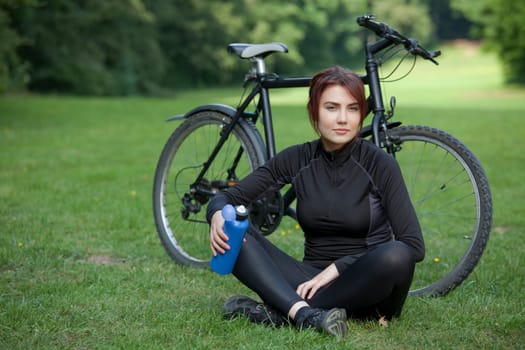 young woman with bike in background resting on the ground
