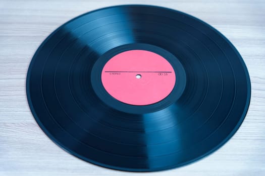 Classic black vinyl record with a red label lying on a wooden background. A nostalgic symbol of analog music, retro sound, and vintage audio formats