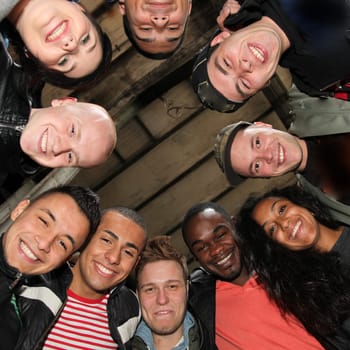 Ten cheerful students of different nationalities stand in a circle and look down laughing