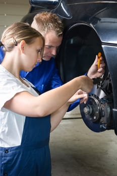 The master craftsman shows the female trainee how to maintain the brakes in the car workshop