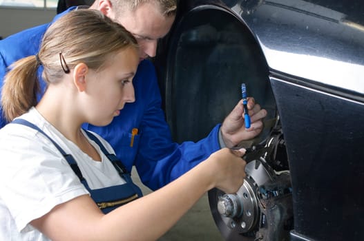 The master craftsman shows the female trainee how to maintain the brakes in the car workshop