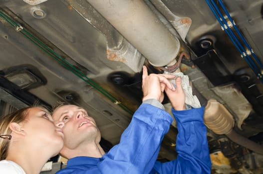 The master mechanic shows the young trainee how to test the exhaust system on the underbody in the car workshop.