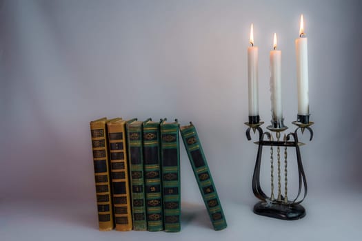 A row of antique hardcover books leaning slightly, next to a vintage candelabrum with burning candles, creating a nostalgic and moody atmosphere