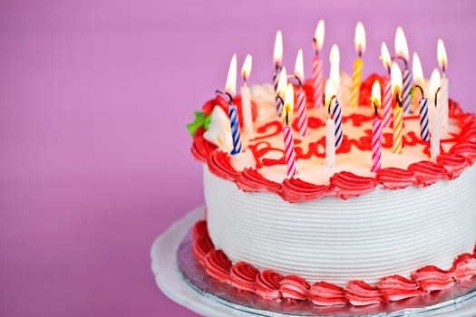 Birthday cake with burning candles on a plate on pink background