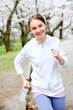 Beautiful teenage girl jogging in park with blooming apple trees
