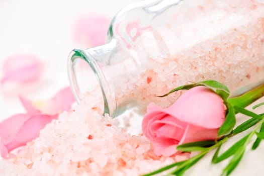 Pink bath salts in a glass jar with flowers and herbs