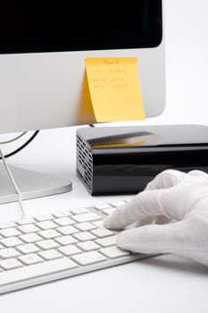 Social engineering concept - man with protective gloves steal data from computer to his external hard disc, fictitious logins and passwords on sticky notes