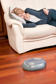 Woman looking at home washing robot in cleaning action, saving her time. Genuine living room wooden floor (jatoba). Selective focus on robot.