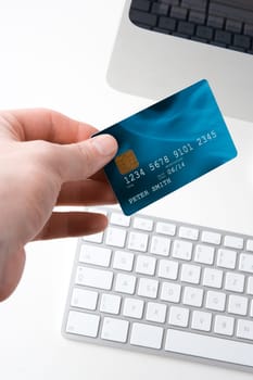 Hand with credit card and computer - electronic payment concept. Focused on credit card. I am author of image used on credit card and used data are fictitious.