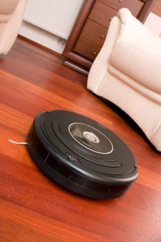Close-up home vacuum cleaning robot in action on genuine living room wooden floor. Selective focus on robot.