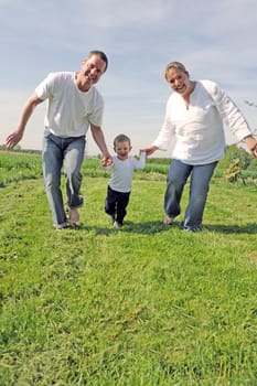 Young family with toddler running together across the field