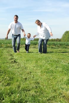 Young family with toddler running together across the field