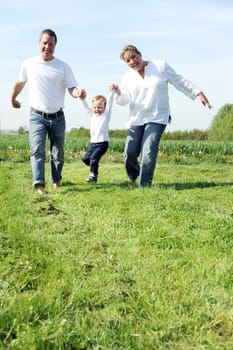 Young family with toddler running together across the field