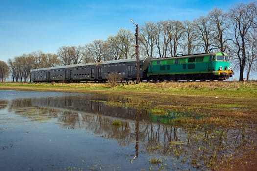 Passenger train hauled by the diesel locomotive passing the sunny landscape