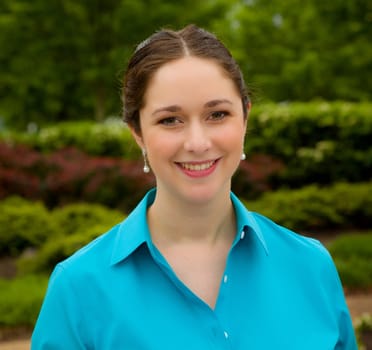 Young lady with nicely made-up face smiles gently at the camera in a garden setting with the flowers lightly blurred