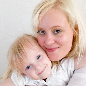 Head portrait of young blonde mother with blonde four-year-old daughter with faces touching sideways