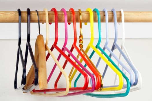 A colorful variety of clothes hangers on a wooden rod.