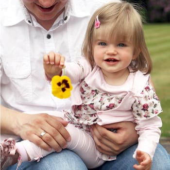 Young father with child. The child holds a flower towards the camera - square