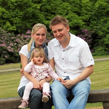 Young family with child in the park. The family sits on a park bench and laughs squarely