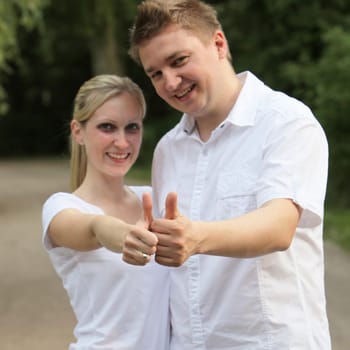 Young couple holding thumbs up while smiling - square