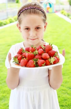 Cute girl holding plate of fresh strawberries
