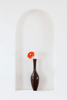 Vase with a single red flower on a wall alcove