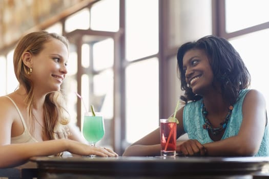 african and latin american female friends drinking cocktails and talking in a pub. Horizontal shape, side view, waist up