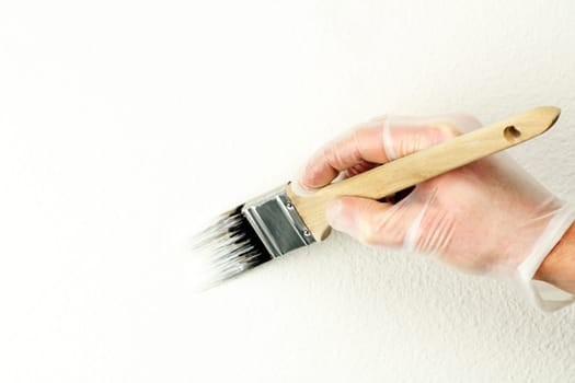 Home touch up painting off-white paint on wall with one and a half inch brush by vinyl gloved hand.