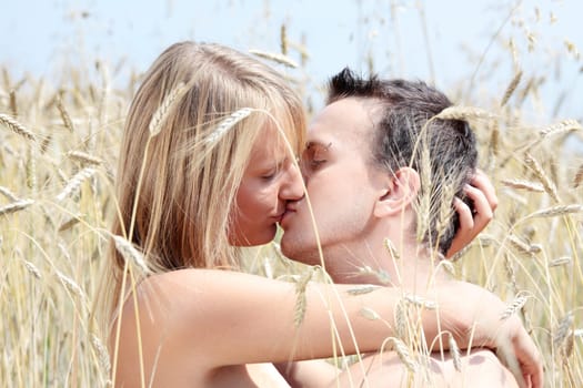 A beautiful couple sitting an kissing in wheat field