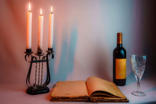 An open vintage book with yellowed pages, an antique candelabrum with burning candles, a wine bottle, and a glass, set in warm dim lighting, creating an elegant and mysterious atmosphere