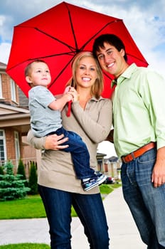 Young happy family under umbrella on sidewalk