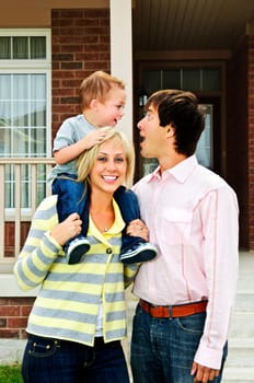 Young happy family standing in front of new home