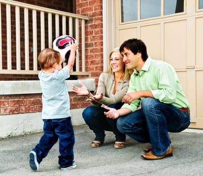 Happy young family playing soccer with toddler on driveway